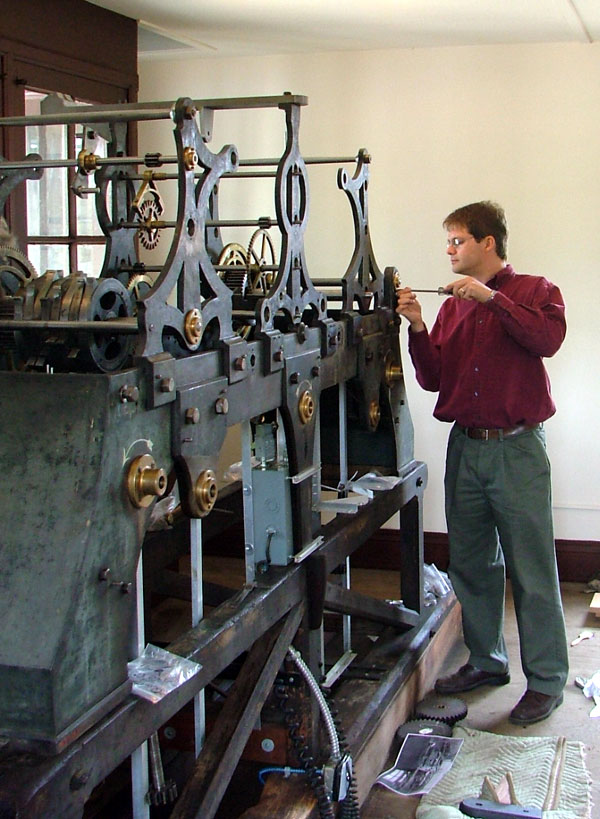 Reassembling the clock movement Man using a screwdriver on a large and elaborate piece of machinery