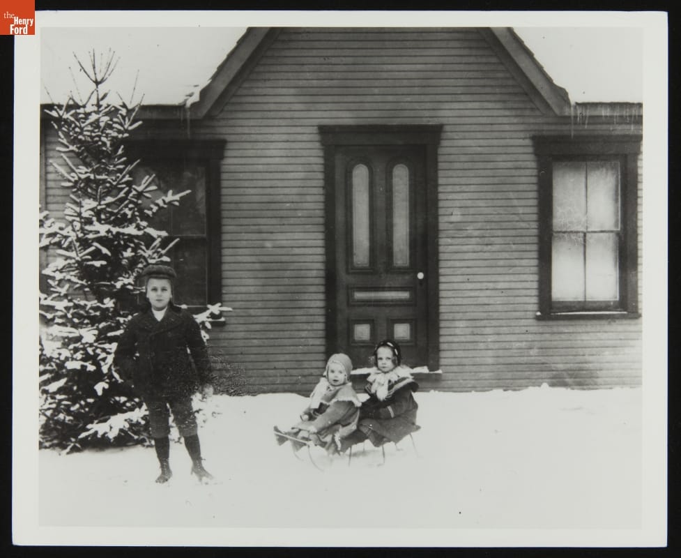 Milton, Leontine, and Ivonette Wright at Wright Home, Dayton, Ohio, circa 1900 Two children sit on a sleigh in snow in front of a door; another boy stands nearby in front of a tree