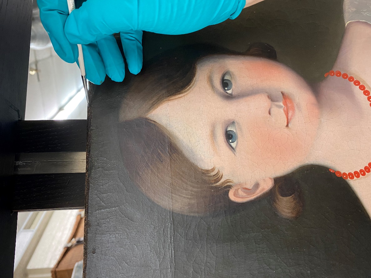 Conservator inpainting Blue-gloved hand holds a paintbrush at the top of a painting of a girl's head