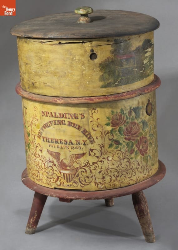 Revolving Beehive, 1869-1877 Yellow, drum-shaped form painted with text and decorations, on wooden stool with three legs