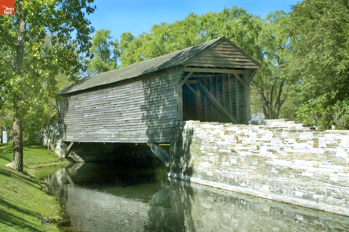 Ackley Covered Bridge A wooden covered bridge crosses a stream with a stone wall on one side and trees behind it