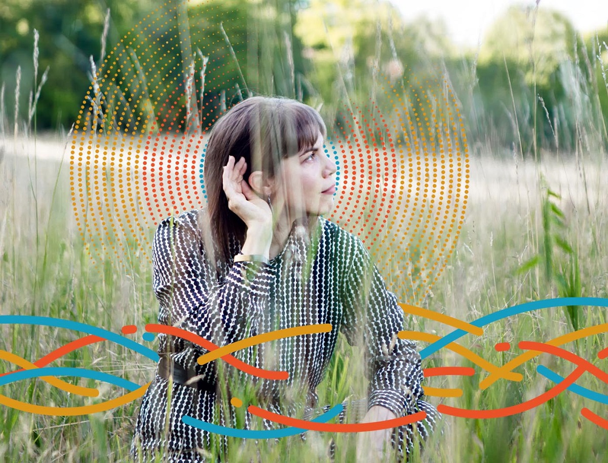 Lavender Suarez Woman in black-and-white printed outfit sits in field with hand to her ear