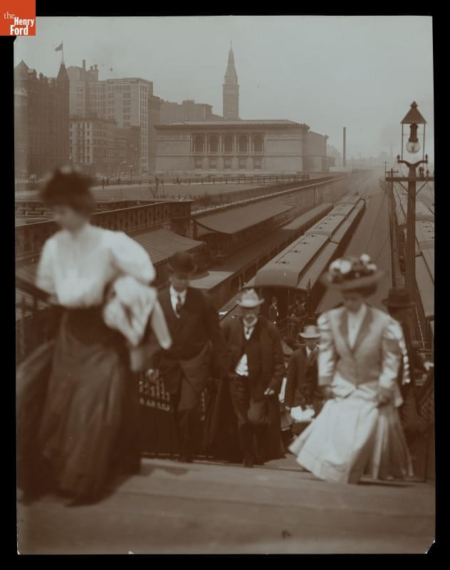 Illinois Central Railroad Station in Chicago, Illinois, circa 1907 People climb a staircase up from sunken railroad tracks with trains on them; buildings in background