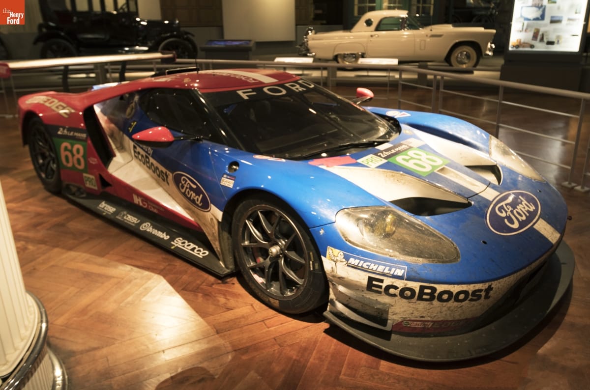 2016 Le Mans Class-winning Ford GT Race Car, On Loan from Ford Motor Company Low blue, red, and white race car with text and logos, sitting in a large indoor space with other cars nearby