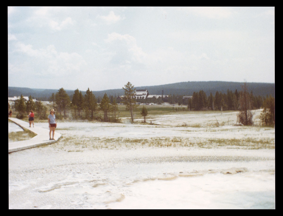 Donna Braden at Yellowstone National Park in 1985 Person stands on boardwalk over white sand or salt with trees and a building in the background