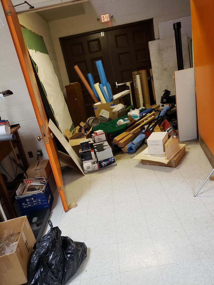Piles of items to donate, sell, or discard Space by large doubledoor cluttered with rolls, boxes, and other items