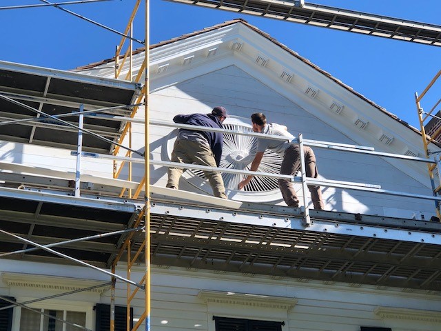 Noah Webster Home ellipse being reinstalled in the pediment Two men on scaffolding hold a large wooden architectural element on a building façade