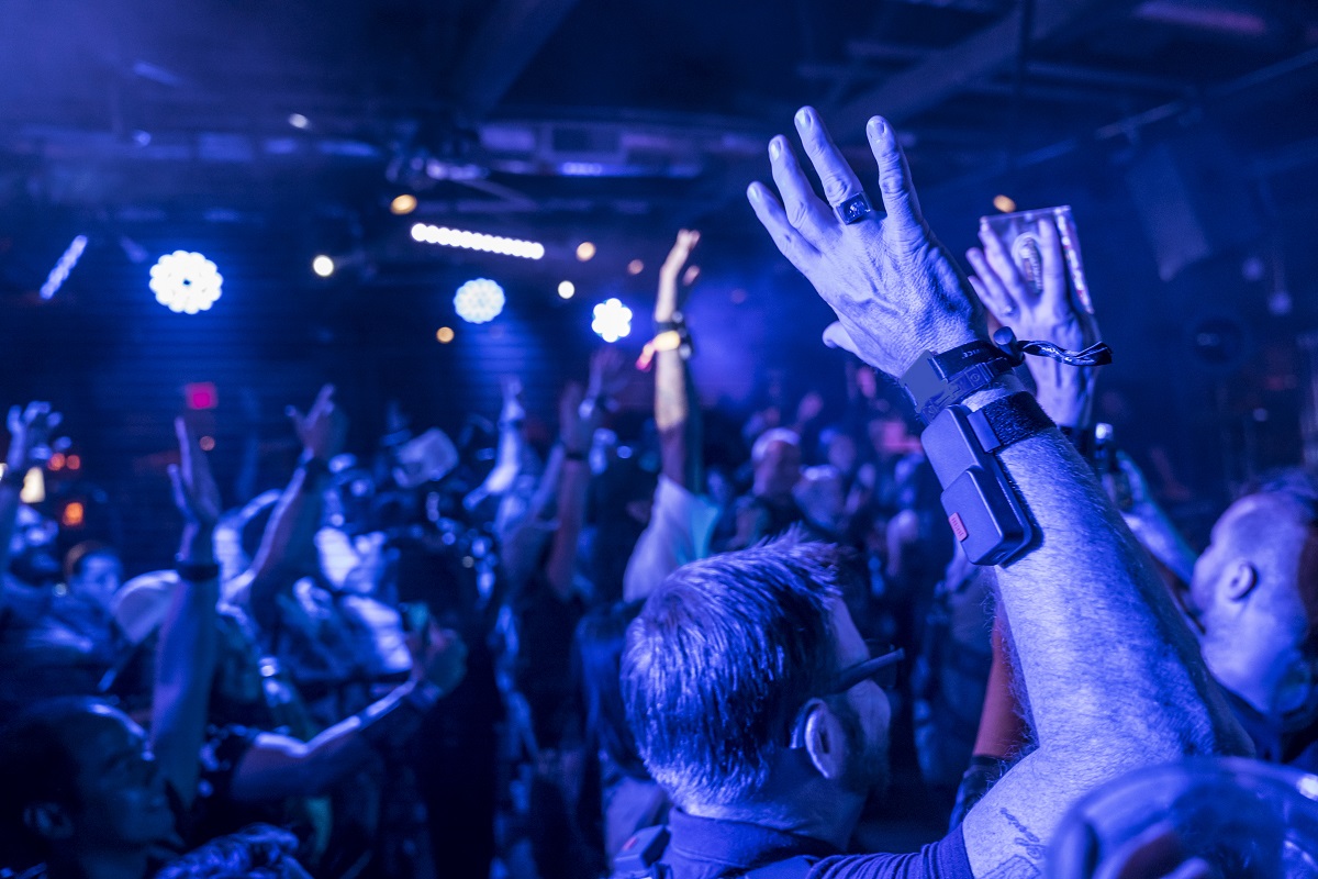 Using the Music Not: Impossible device Room filled with blue light and people with their hands in the air; one close to camera wears a device strapped to his arm
