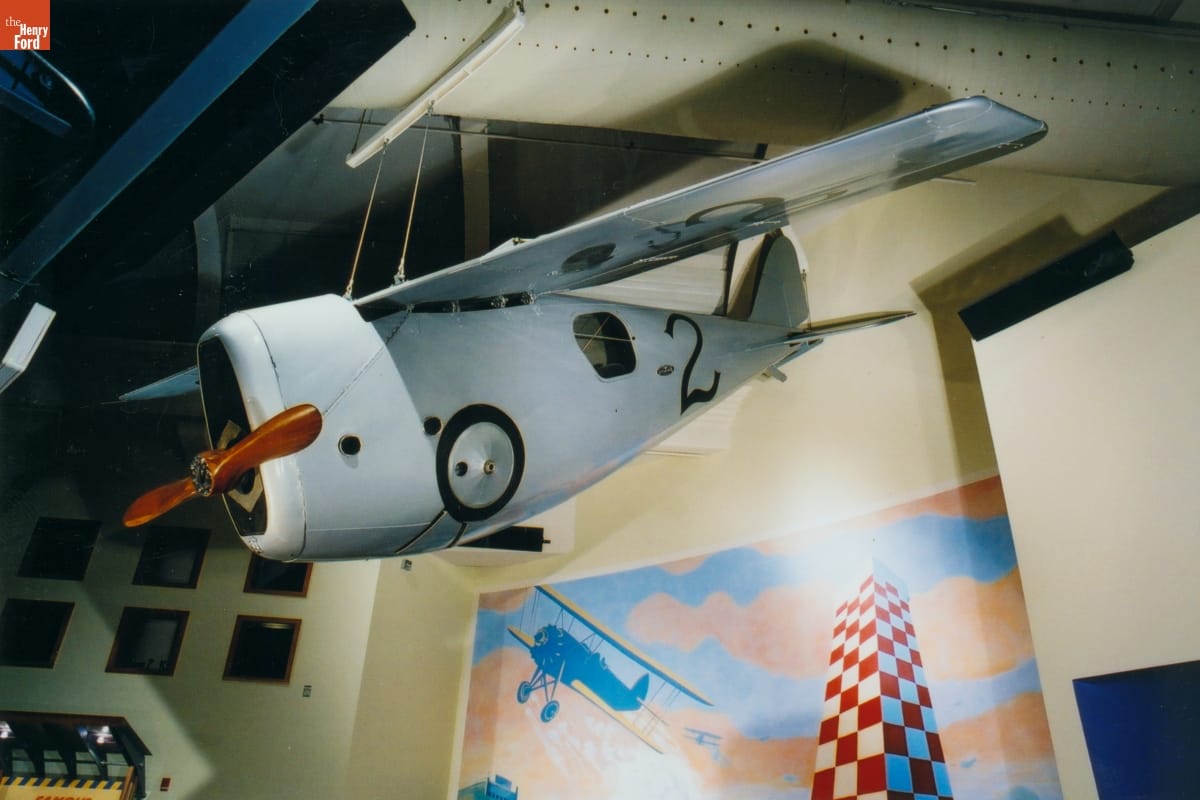 1920 Dayton-Wright RB-1 Monoplane Small silver plane suspended from the ceiling in a room containing painted backdrops on the walls and other objects