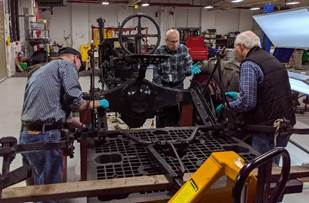 Three men wearing blue gloves work on a piece of equipment