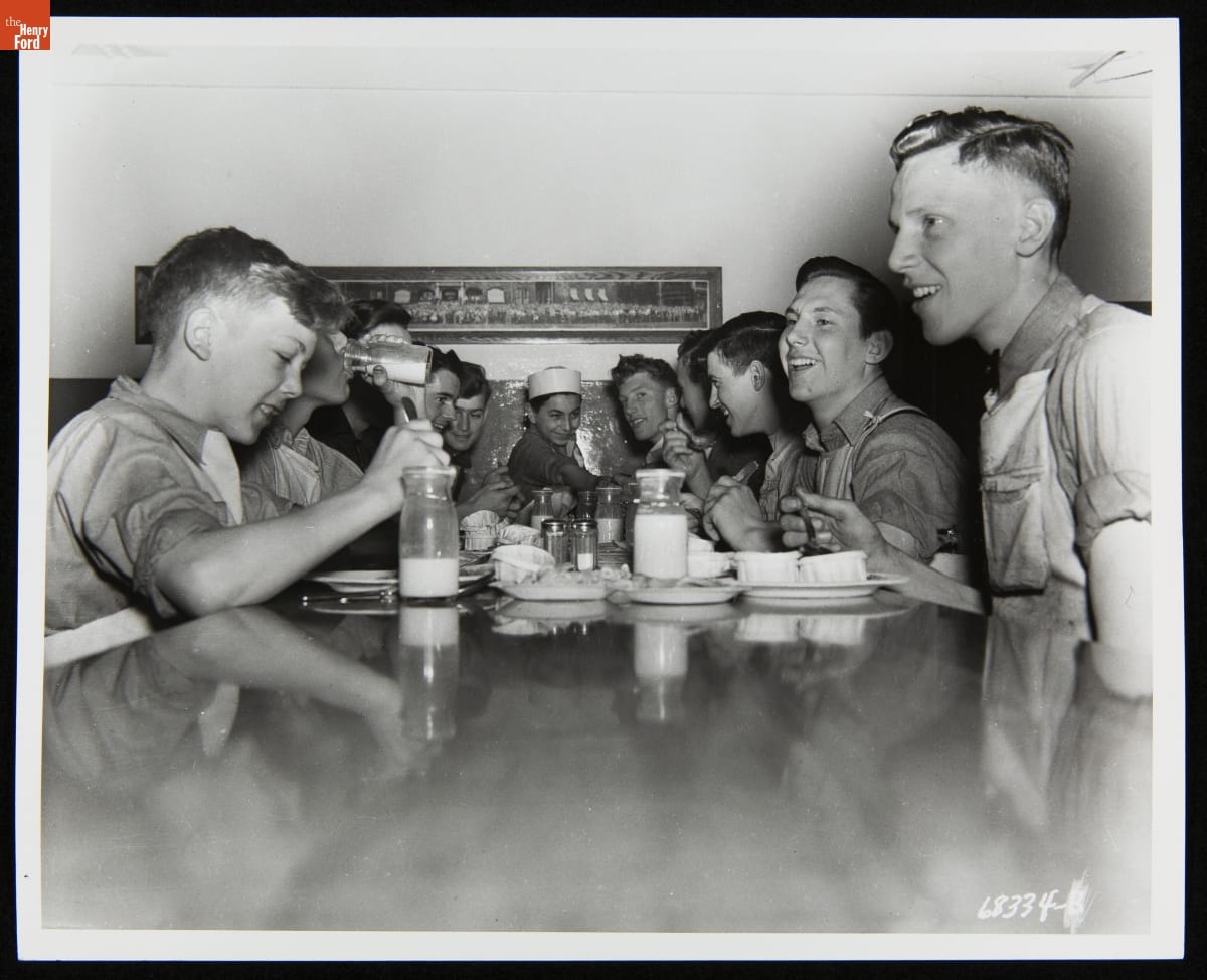 Henry Ford Trade School Students Eating Lunch, May 24, 1937 Group of boys crowd at one end of a dining table with plates and milk bottles on the table in front of them