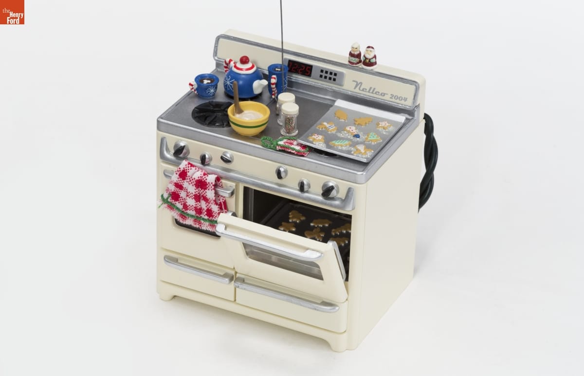 https://www.thehenryford.org/collections-and-research/digital-collections/artifact/492412#slide=gs-498588 Ornament of cream-colored stove with one oven door cracked to show a tray of cookies inside; another tray of cookies, a bowl of dough, and a teapot and two mugs of hot chocolate are on top of stove
