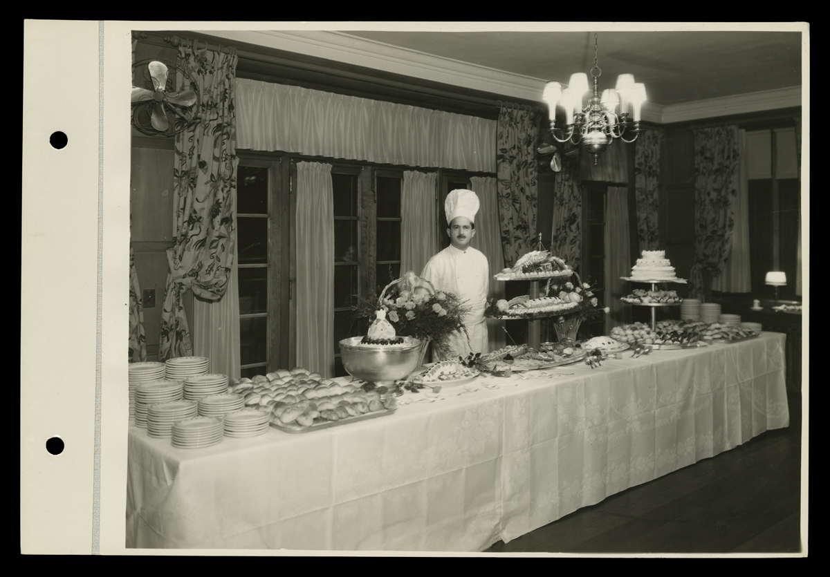 Chef at Banquet Table, Dearborn Country Club, Dearborn, Michigan, 1931 Man in chef's outfit and hat stands behind long buffet table filled with plates and displays of food