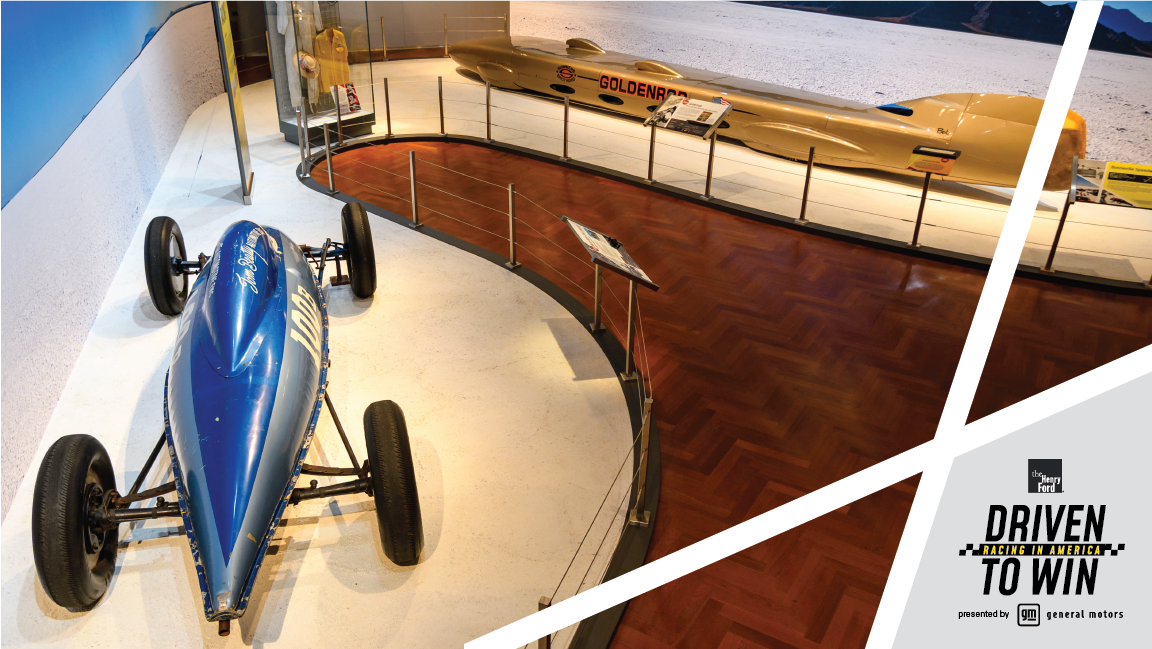 Aerial view of museum exhibit featuring very long, low gold race car and short, squat teardrop-shaped race car in two shades of blue