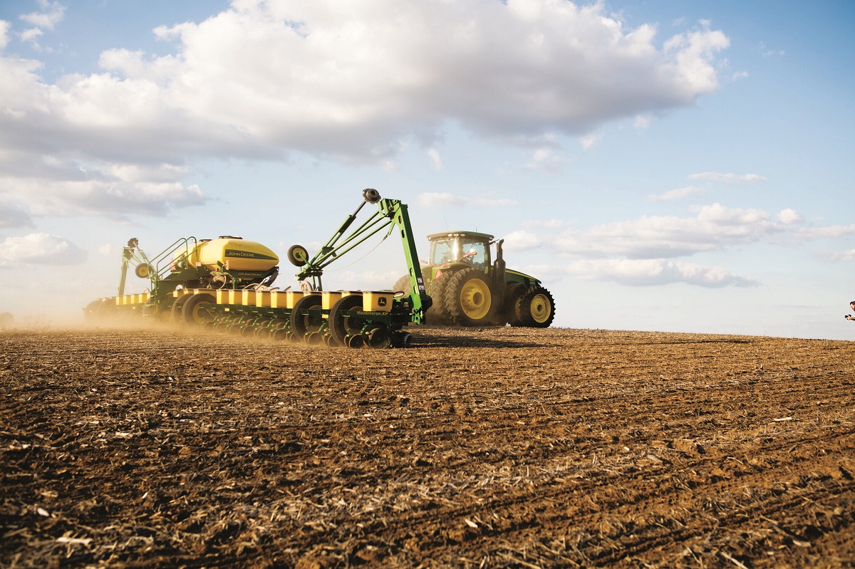John Deere Tractor and Planter Planting Soybeans Green and yellow tractor pulls wide attachment across a dirt field