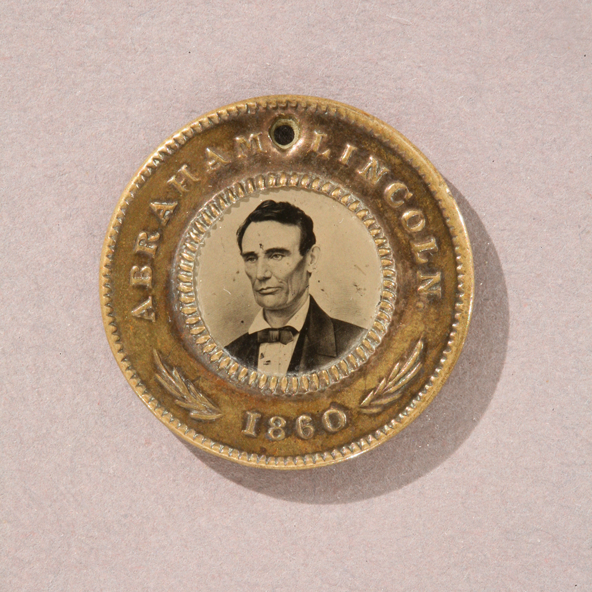 Abraham Lincoln and Hannibal Hamlin Campaign Button, 1860 Round gold token with image of man’s shoulders and head in the middle and text “Abraham Lincoln 1860” around edge