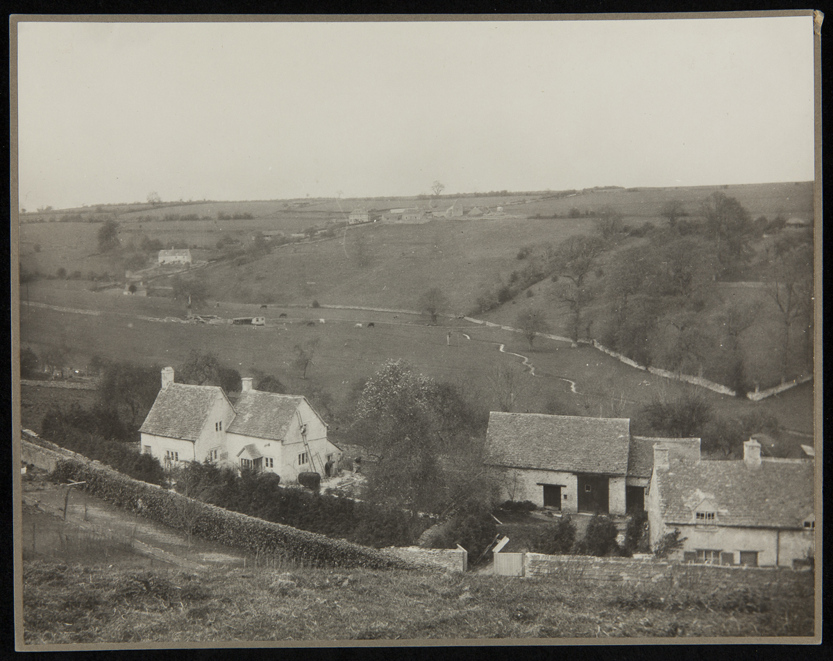 Exterior of Cotswold Cottage at its Original Site, Chedworth, Gloucestershire, England, 1929-1930 Low stone houses and fences among rolling meadows