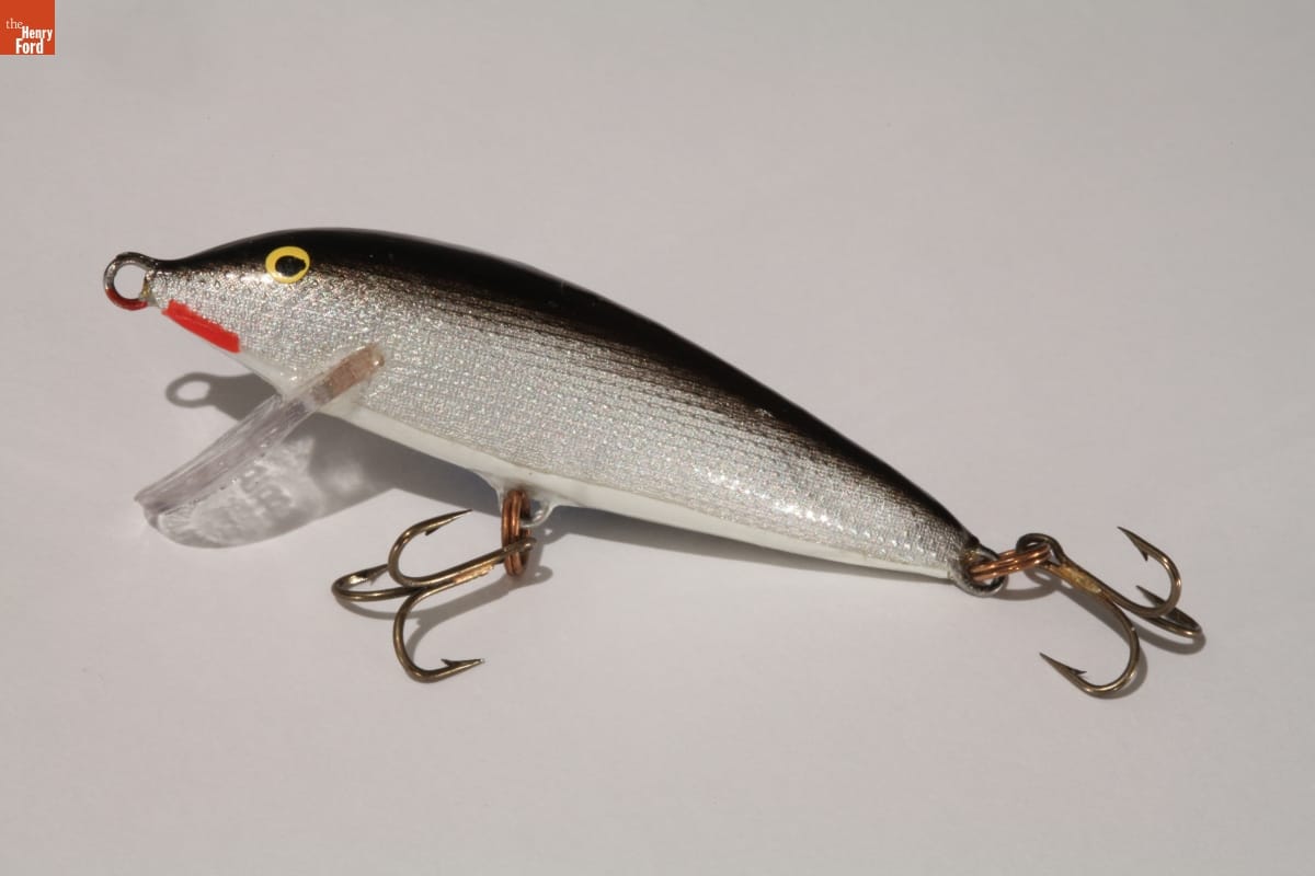 Lure shaped and colored like a fish, with three-pronged hooks hanging from the tail and belly
