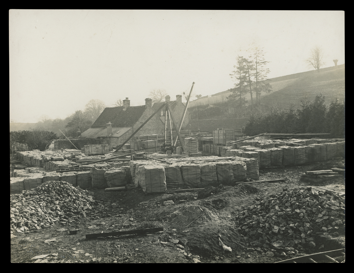Dismantling Cotswold Cottage at its Original Site in England, 1929-1930 Construction site with piles of loose stones and many pallets; stone building in background