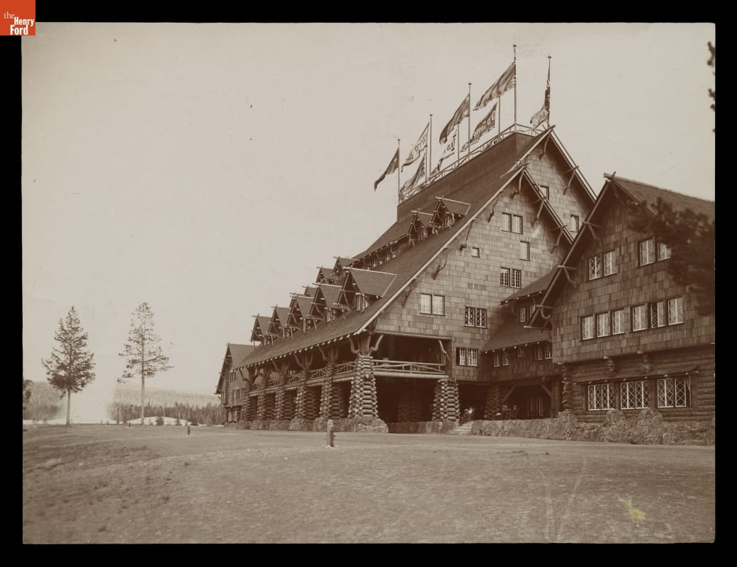 Old Faithful Inn, Detail View of N.W. Entrance, Yellowstone Park, 1905 Black-and-white image of rustic building with steep roof, many gables, and flags at the top of the roofline