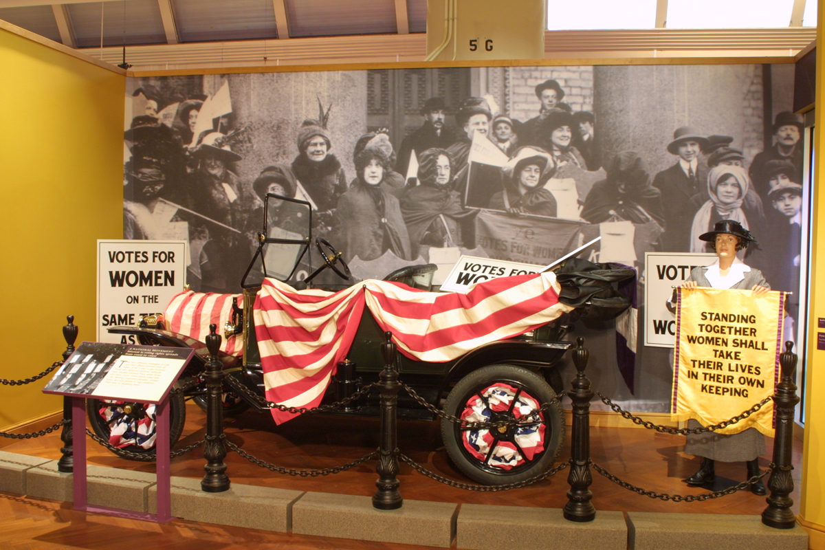 "Votes for Women" Section of "With Liberty and Justice for All" Exhibit in Henry Ford Museum, January 2006 Model T covered in red and white striped bunting, in front of a photograph of women's suffrage advocates