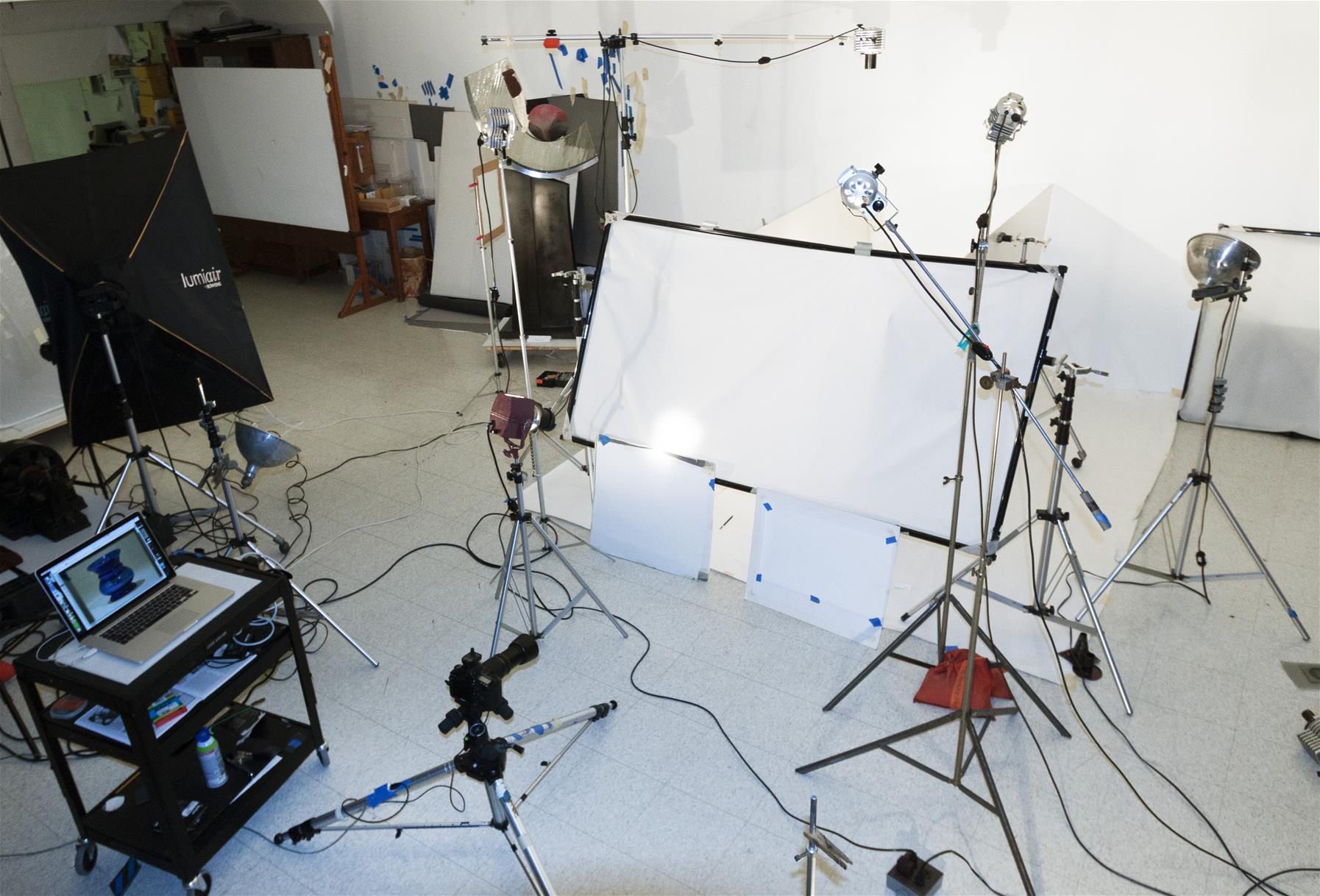 The Henry Ford's Photo Studio set up to photograph a glass spittoon Photo studio with cart with laptop, many lights on stands, area blocked off with white paper
