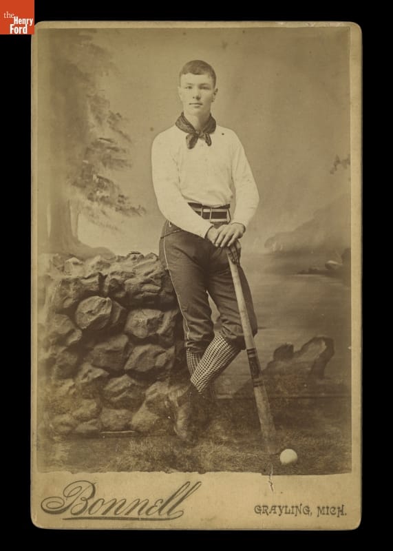 Studio Portrait of a Baseball Player in Uniform, 1885-1889 Black-and-white photo of man in early baseball uniform holding baseball bat, leaning on a stone wall in front of a backdrop