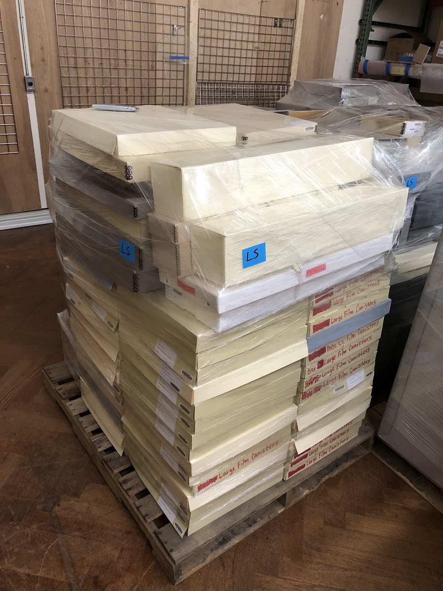 Material from Lillian Schwartz collection at The Henry Ford Pallet containing many wide, shallow boxes, all wrapped in clear plastic wrap, sitting in a storage area among other similarly packaged material
