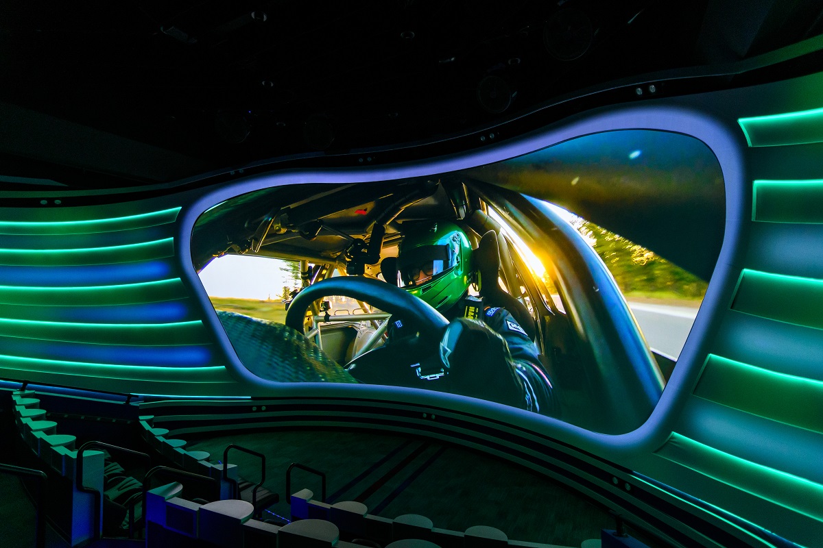 The Driven to Win multisensory theater in Henry Ford Museum of American Innovation. Curved theater with visor-shaped image of race car driver on screen and blue and green bars extending outward