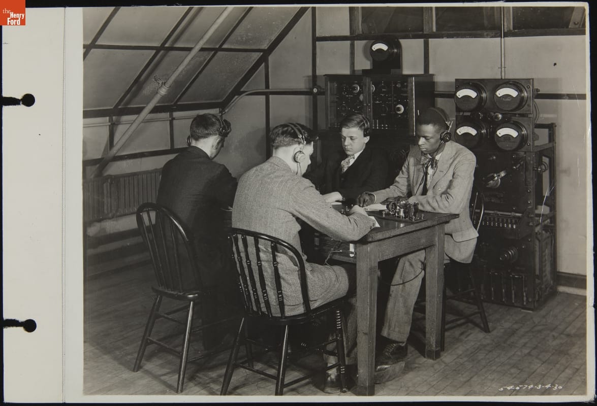 Claude Harvard with Other Radio Club Members, Henry Ford Trade School, March 1930 Four men in suits wearing headphones sit at a table with equipment on the table and along the wall behind them