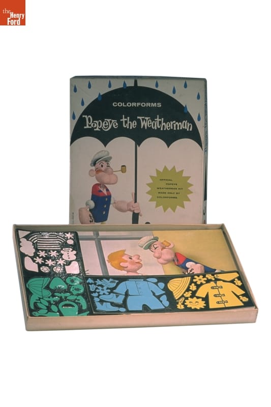 Colorforms Set, Popeye the Weatherman, 1959 Open box with lid standing on end behind it; box contains colorful pieces on a sheet; box lid contains image of sailor Popeye character with umbrella and text