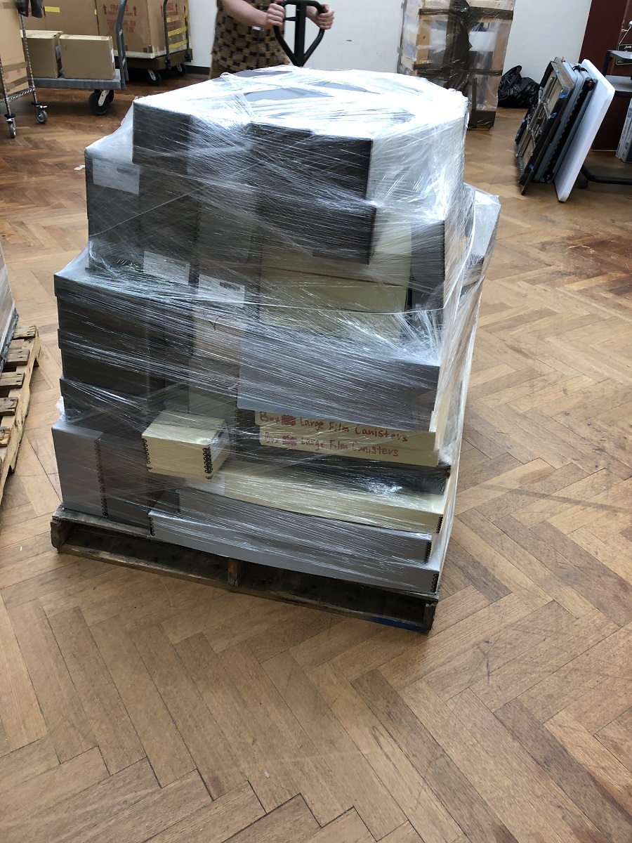 Wrapped pallet of Lillian Schwartz collection material at The Henry Ford Pallet filled with boxes, all wrapped with clear plastic, sitting in storage area among other boxes and pallets