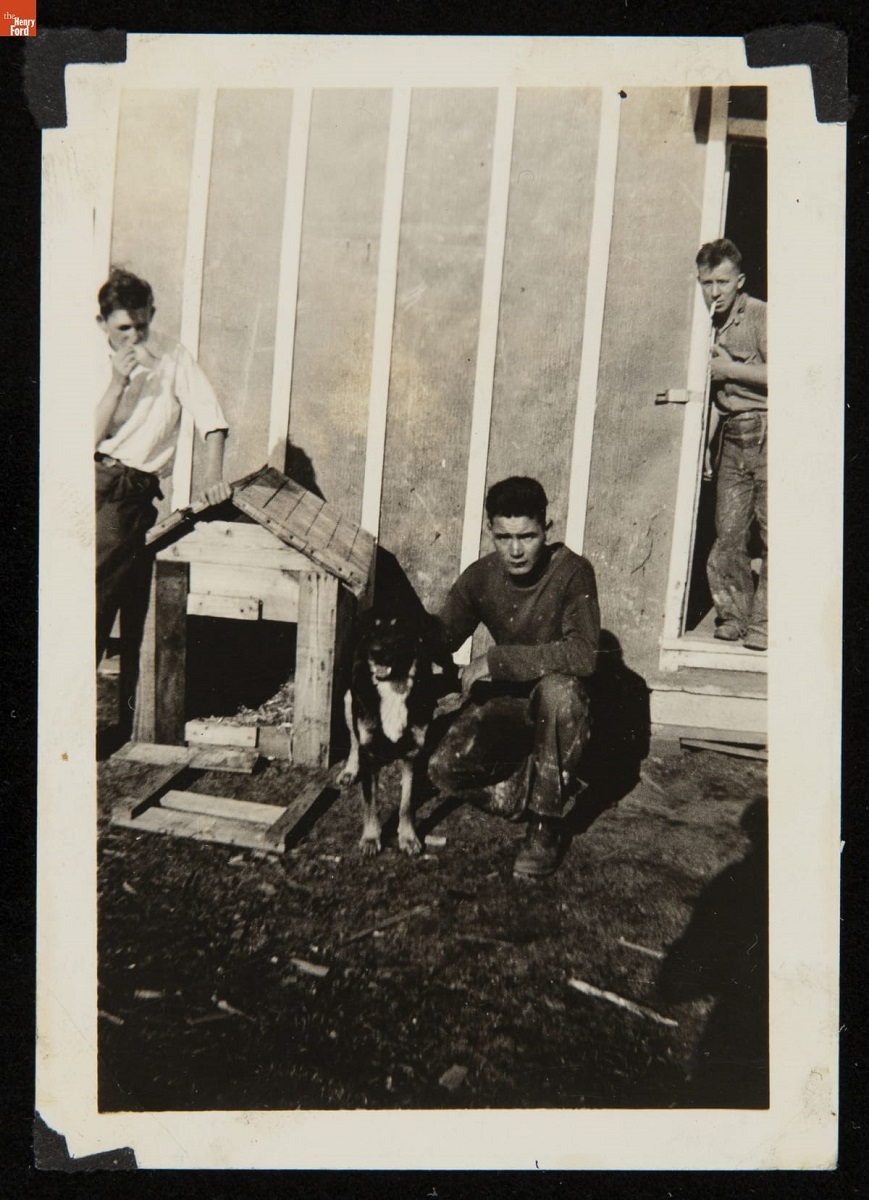 Stanley Zaleski and a Dog outside Civilian Conservation Corps Barracks, 1934 Man kneels with dog next to doghouse; other men stand nearby