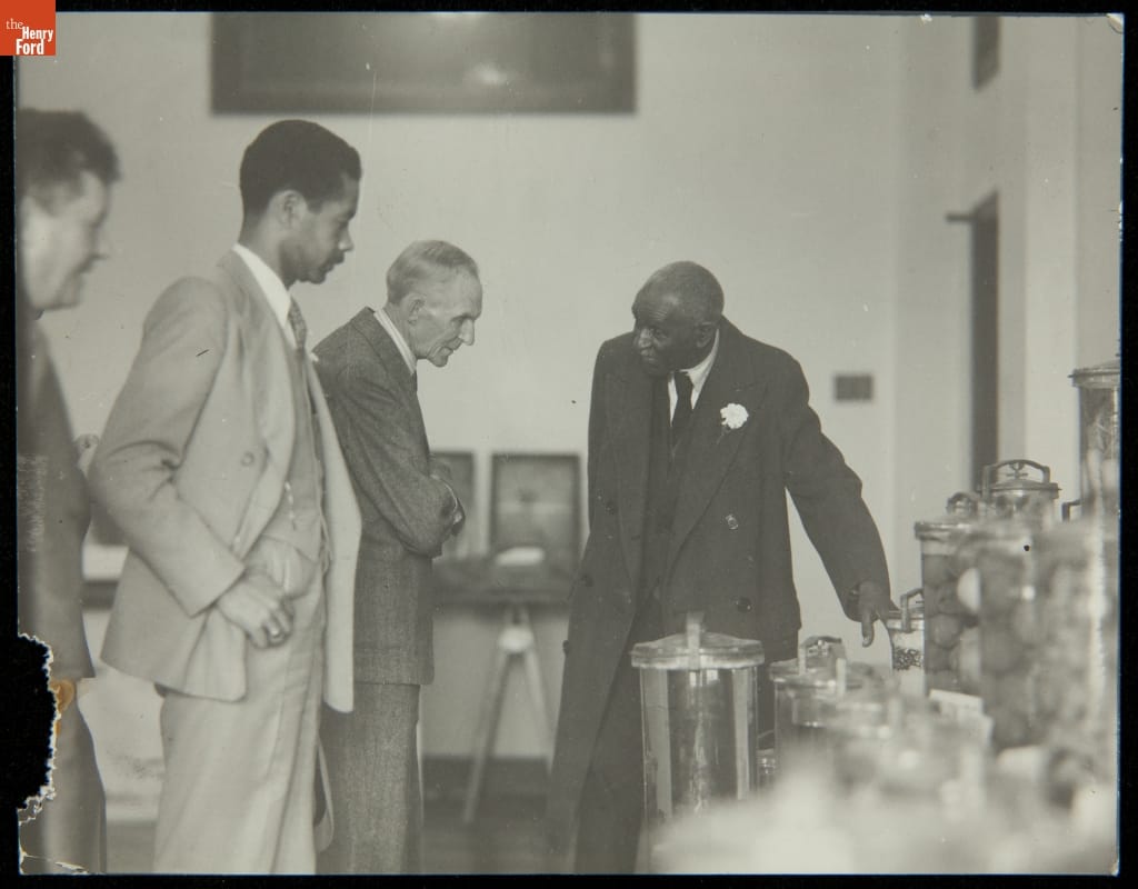 Man gestures to a table covered in glass jars while other men look on