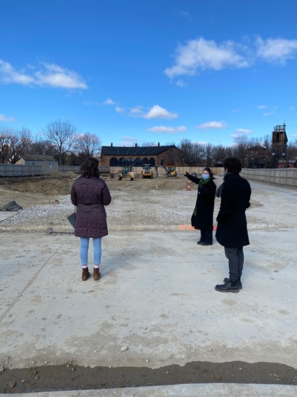 Ayana Curran-Howes, Debra Reid, and Antonello Mastronardi at the site where the Vegetable Building is being reconstructed in Greenfield Village Two people look at a construction site, while a third in a mask looks at the first two and gestures toward construction site