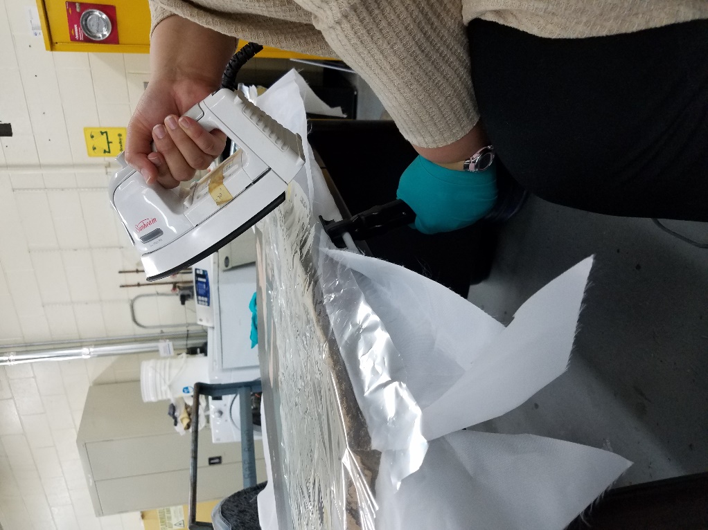 Re-stretching the canvas Person wearing gloves holds an iron to a flat item on a table in a lab