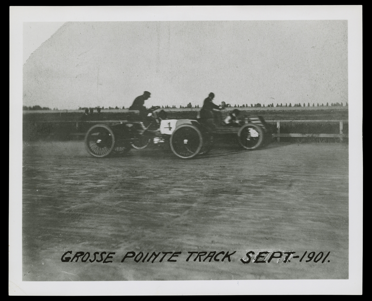 Henry Ford Driving the Sweepstakes Racer Against Alexander Winton, Grosse Pointe, Michigan, October 10, 1901 Two minimalistic early cars with a driver in each on dirt track with fence and grass in background