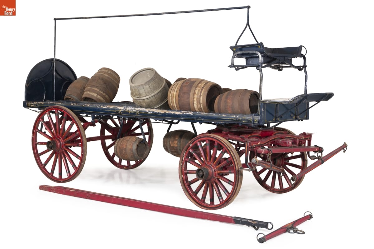Open four-wheeled wagon holding a variety of sizes of wooden kegs
