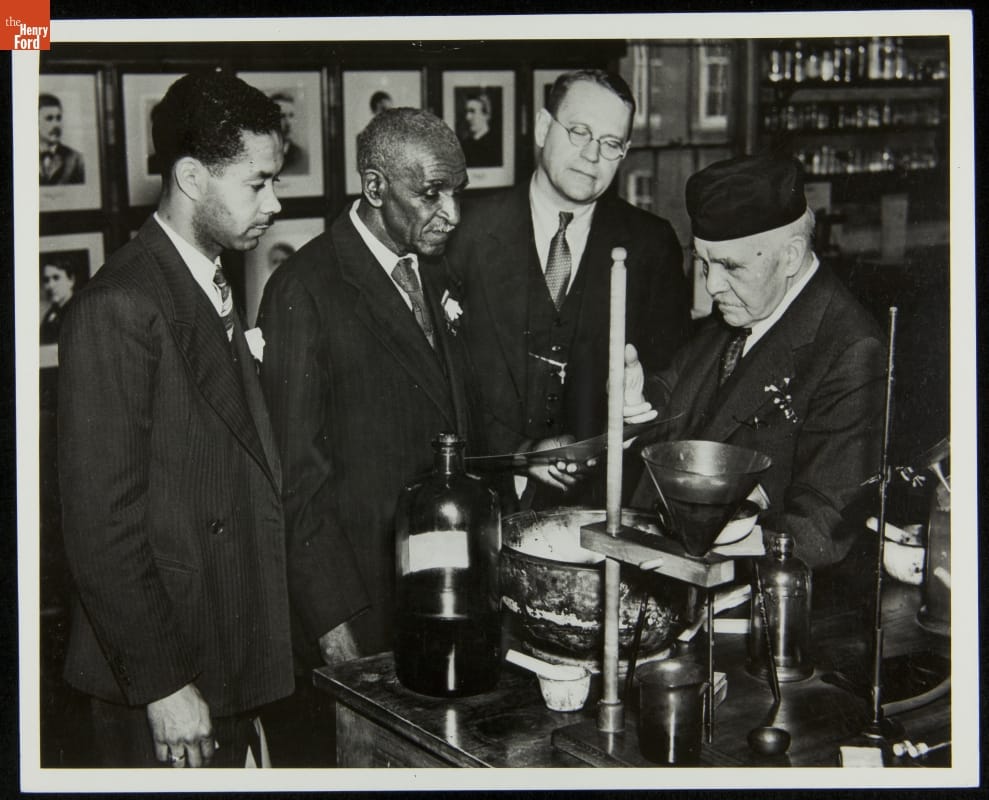 Austin W. Curtis, George Washington Carver, William Simonds and Francis Jehl at Menlo Park Laboratory, Greenfield Village, 1937 Black-and-white image of four men in suits looking at a piece of equipment on a table in a workroom or laboratory