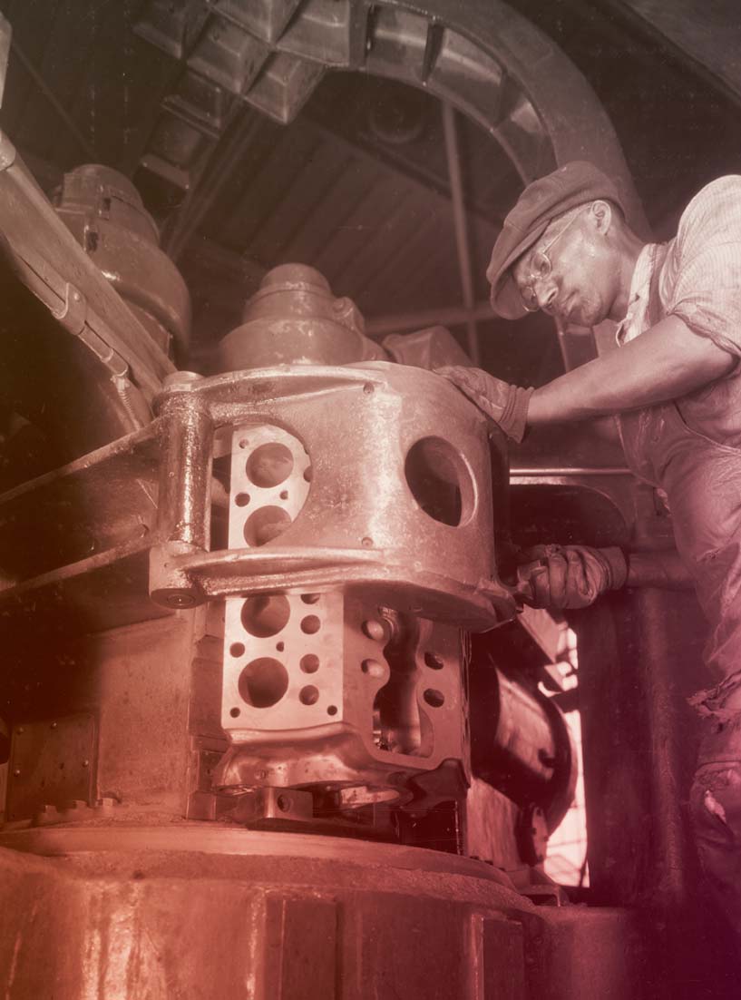Employee in the Rouge Plant Foundry Machine Shop, Working on Ford V-8 Cylinder Blocks, 1934 Man in work clothing and cap works at large piece of equipment