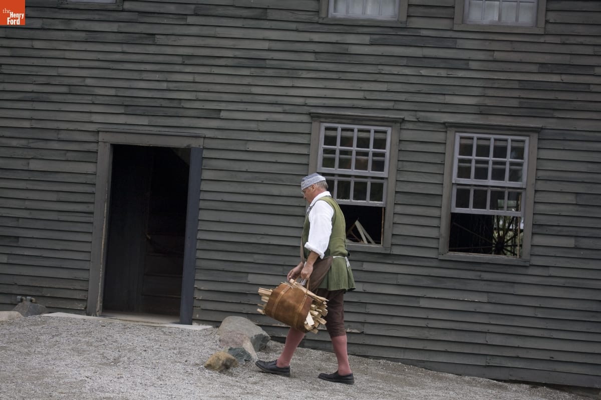 Daggett Farm in Greenfield Village, October 2007, Photographed by Michelle Andonian Man wearing historic clothing walks past simple gray wooden house
