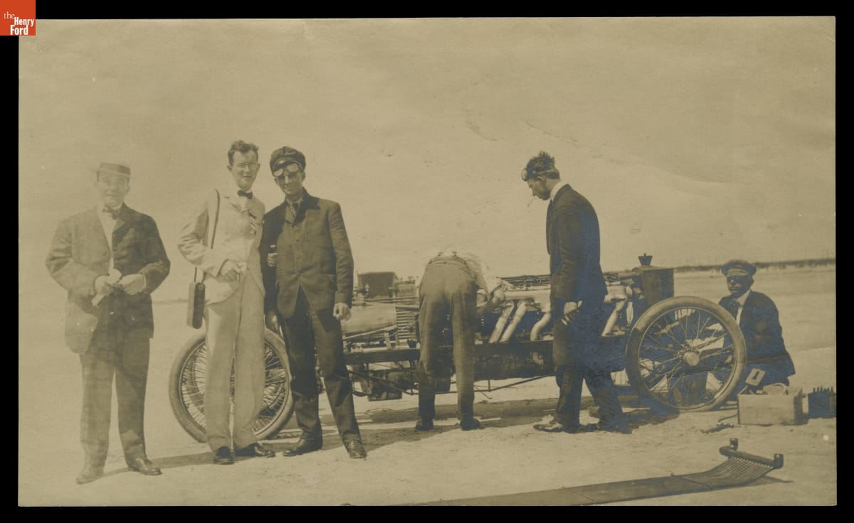 Henry Ford and Frank Kulick with Ford Model K Race Car on Beach in New Jersey, 1905 Black-and-white photo of three men standing near and three men working on early open race car on a beach