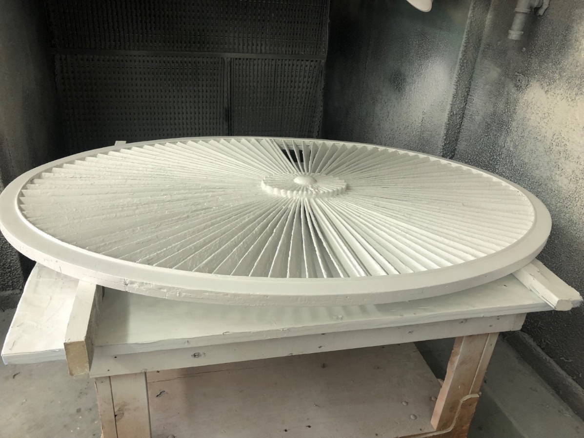 Decorative ellipse from the front pediment of the Noah Webster Home Round decorative architectural detail sitting on work table in space with paint-spattered walls