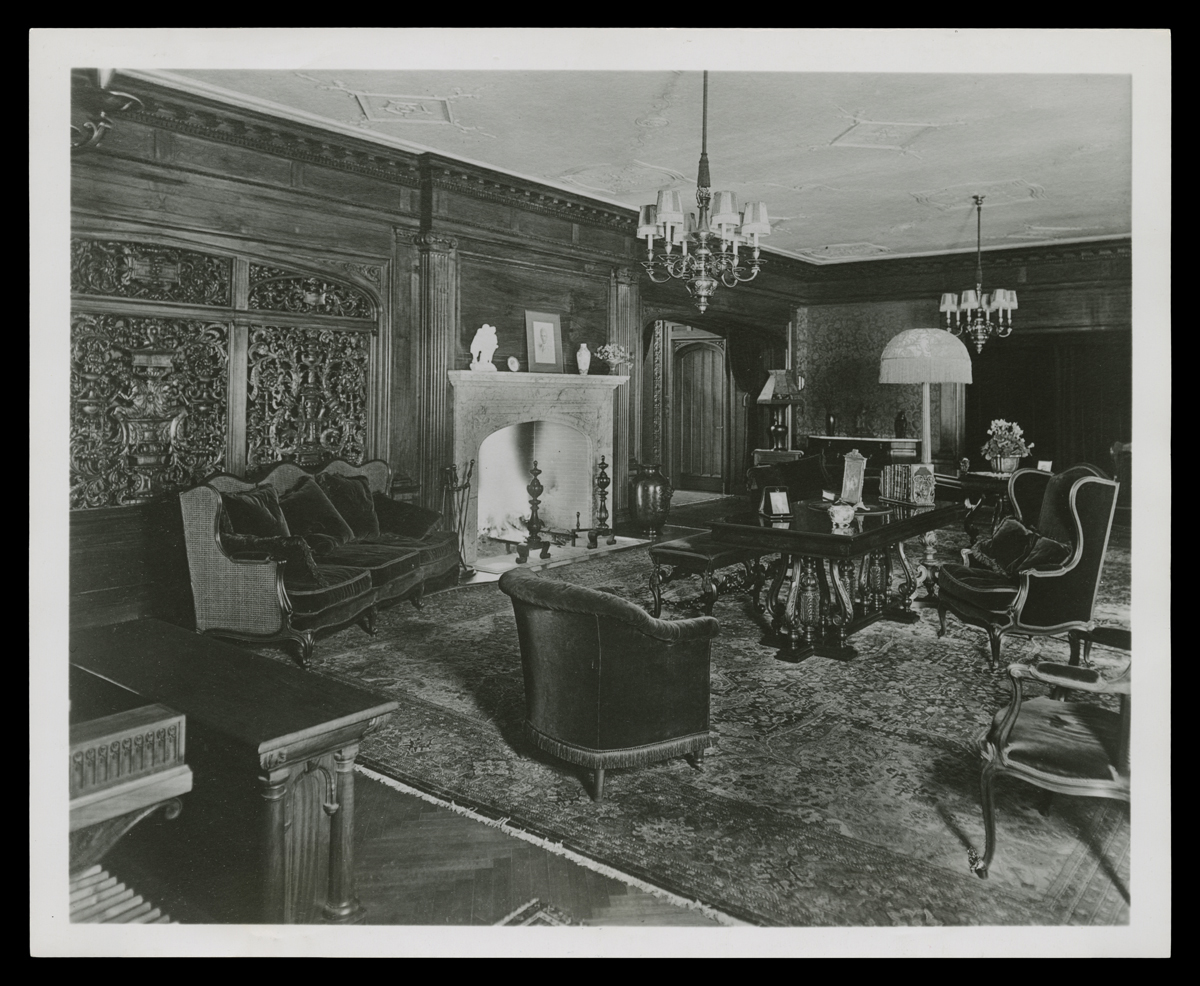 THF132991 Room interior with intricately carved wood and fireplace, filled with upholstered chairs, a table, and other furniture