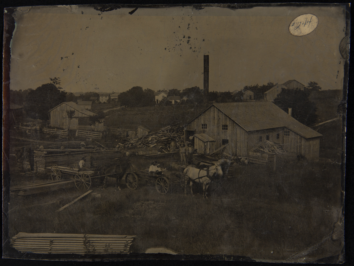Workers and Horse-drawn Wagons at a Sawmill, 1880-1900 Landscape with wooden buildings, stacks and piles of lumber, horses and wagons, and people