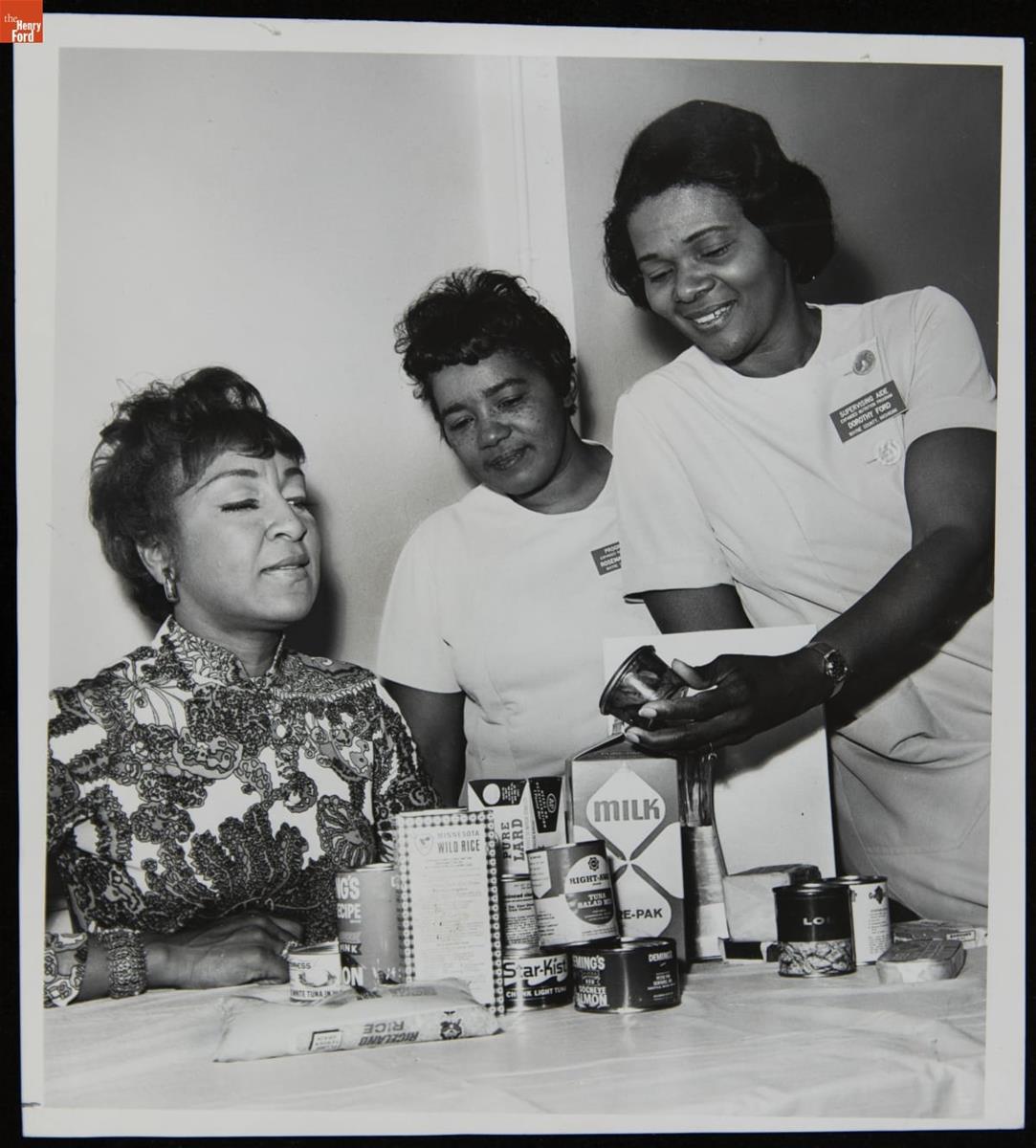 June Sears, Rosemary Dishman, and Dorothy Ford Discussing Women's Nutrition, May 1970 Three women of color standing and sitting around a table containing canned, boxed, and bagged food items
