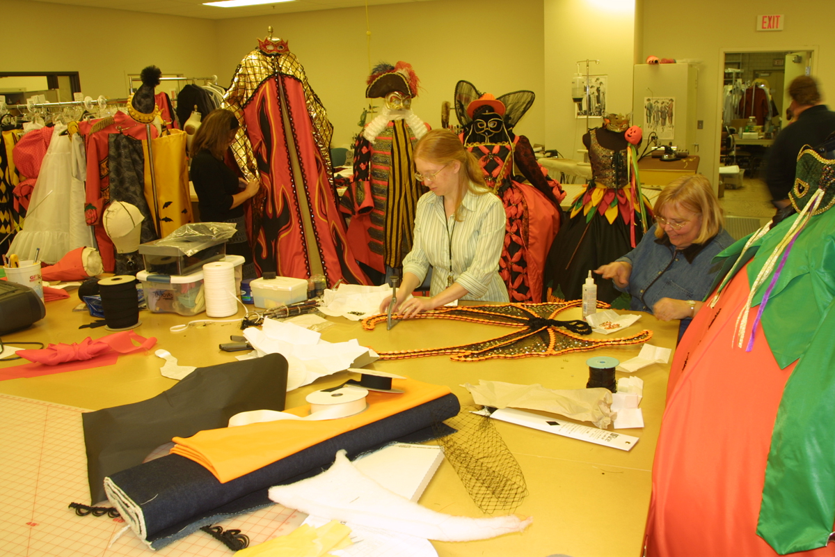 Costume Studio Preparing for Halloween in Greenfield Village, October 2005 Two women work at a large table filled with fabric bolts and sewing notions; elaborate costumes hang in the background