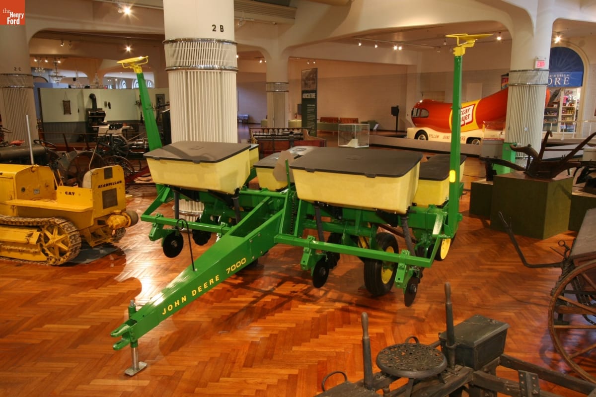 John Deere 7000 No-Till Planter, 1978 Large green agricultural implement with yellow bins, in an exhibit among other agricultural equipment and other objects