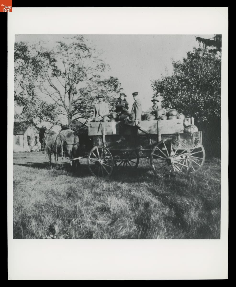 Horse-drawn wagon filled with pumpkins with several people inside