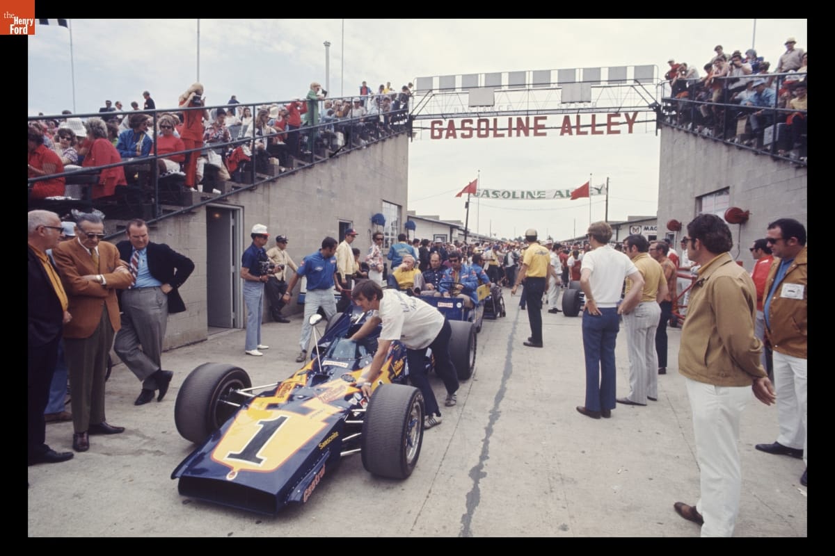 Colt/Ford Race Car Driven by Al Unser in the Indianapolis 500, May 1971 People push racecars through a gap between concrete grandstands filled with people as many watch